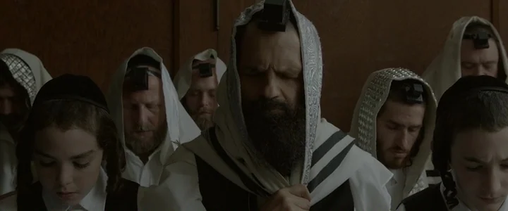 To Dust - Nightmares (2018) movie still: medium — A group of men and boys stand closely together in a wooden-paneled interior space. They wear…