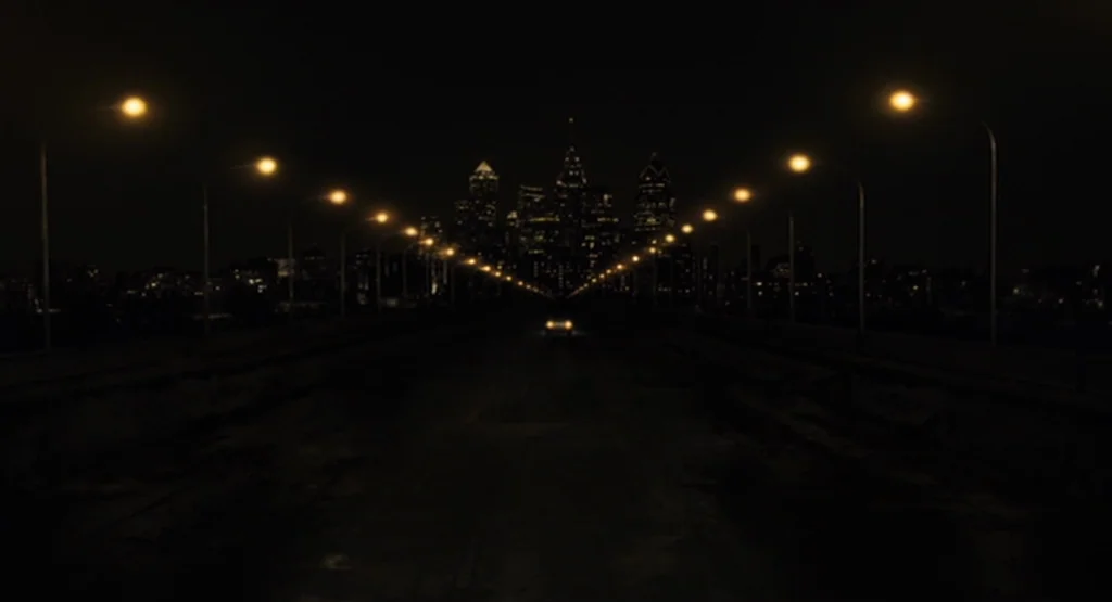 The Fountain (2006) movie still: establishing — A long, dark bridge extends into a distant, brightly lit urban skyline at night. A lone vehicle…