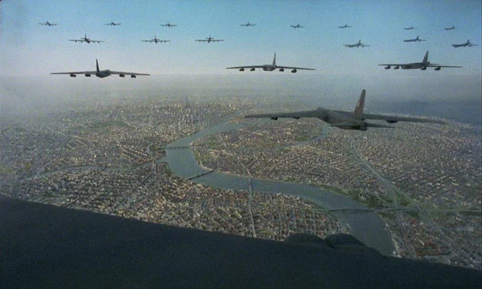 You, The Living (2007) movie still: establishing — A vast aerial view shows a fleet of B-52 bombers flying over a city. A winding river snakes…