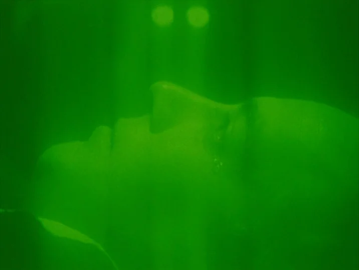 Careful (1992) movie still: closeup — A man lies on his back in a monochromatic green night vision display. He has his eyes closed and is framed in…