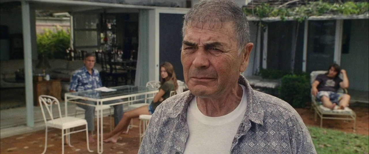 The Descendants (2011) movie still: medium — A residential patio area with a glass-topped table and lounge chairs on paved ground. One older man…