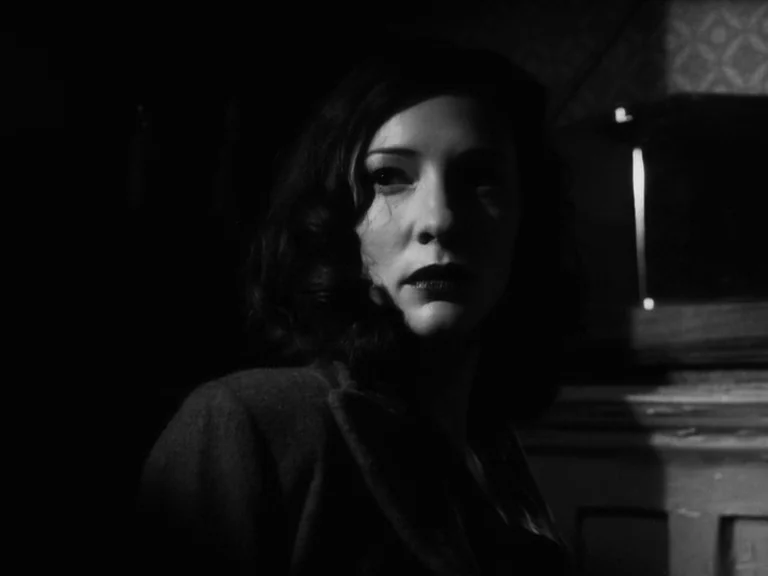 The Good German movie still: closeup — A dim room interior features dark walls and a faint hint of wallpaper pattern. The subject stands in the…