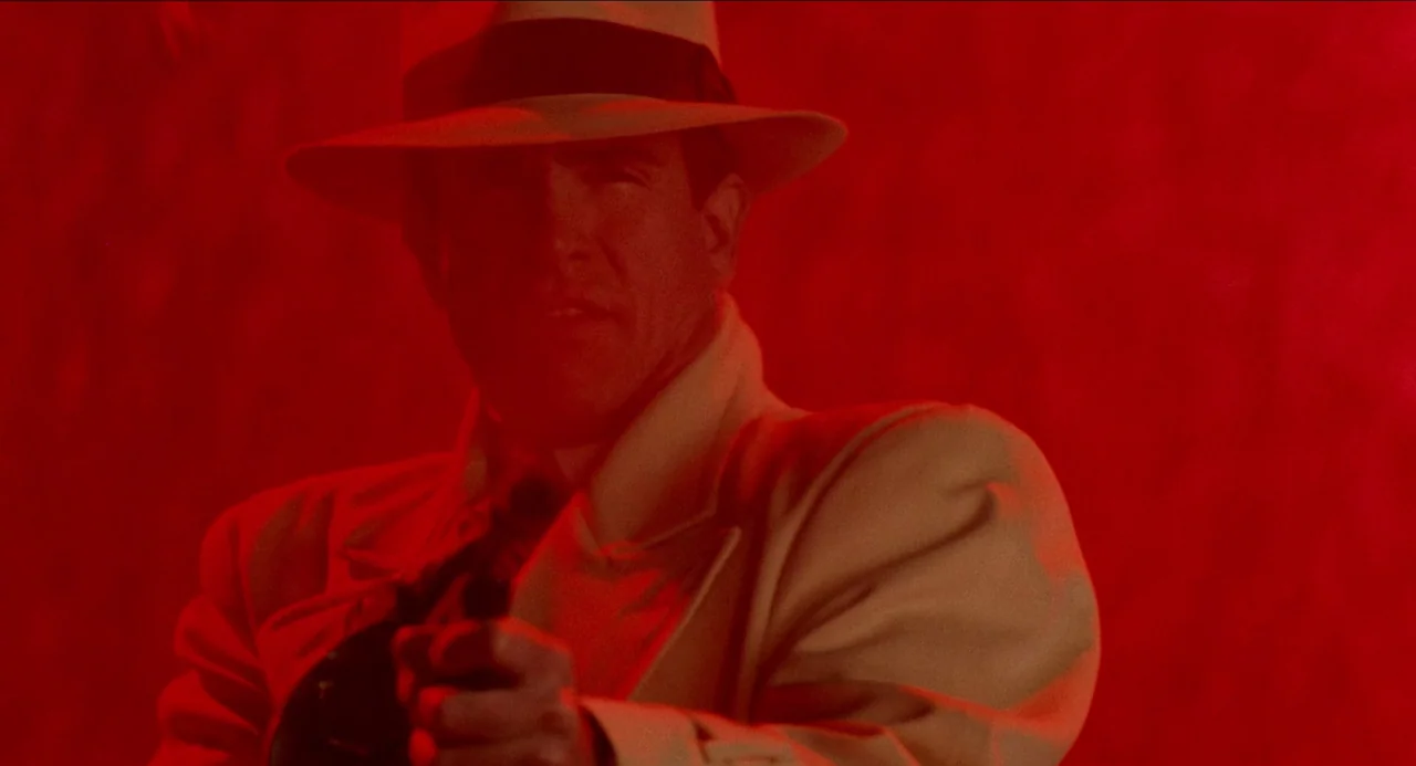 Dick Tracy (1990) movie still: medium — A man stands in an environment completely flooded with intense red light. He wears a fedora and trench coat…
