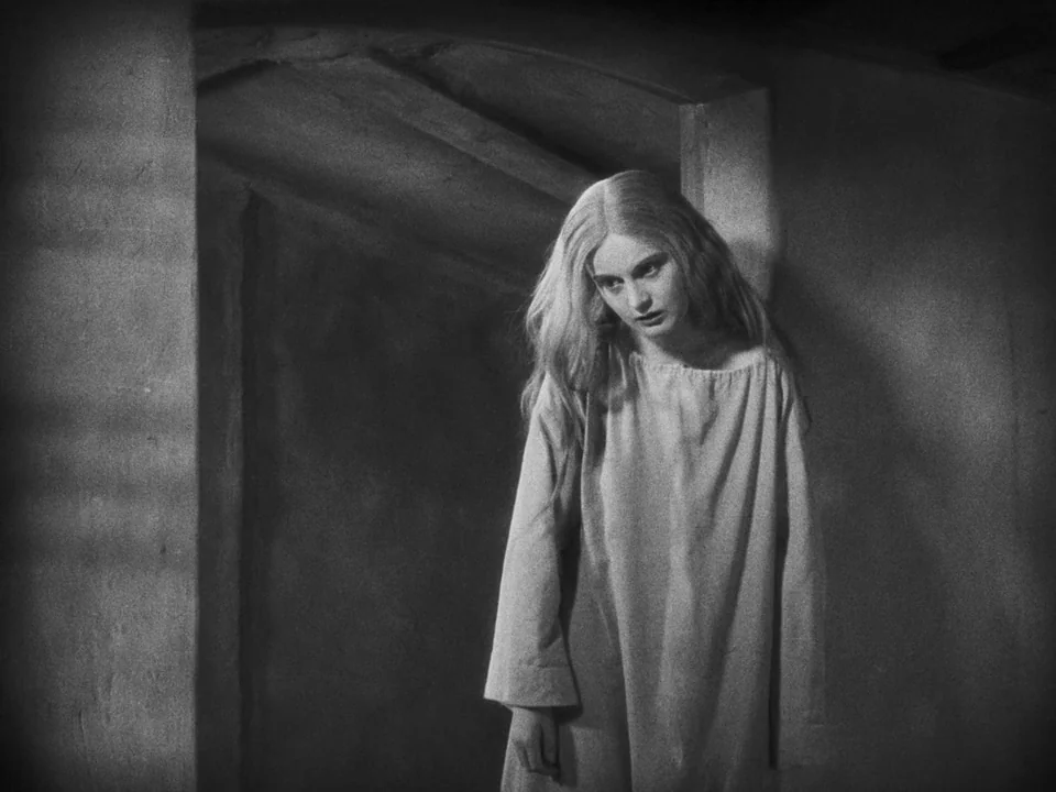 Faust (1926) movie still: medium — A dark stone interior featuring a vaulted doorway with rough-hewn walls. A young woman stands in the entrance,…
