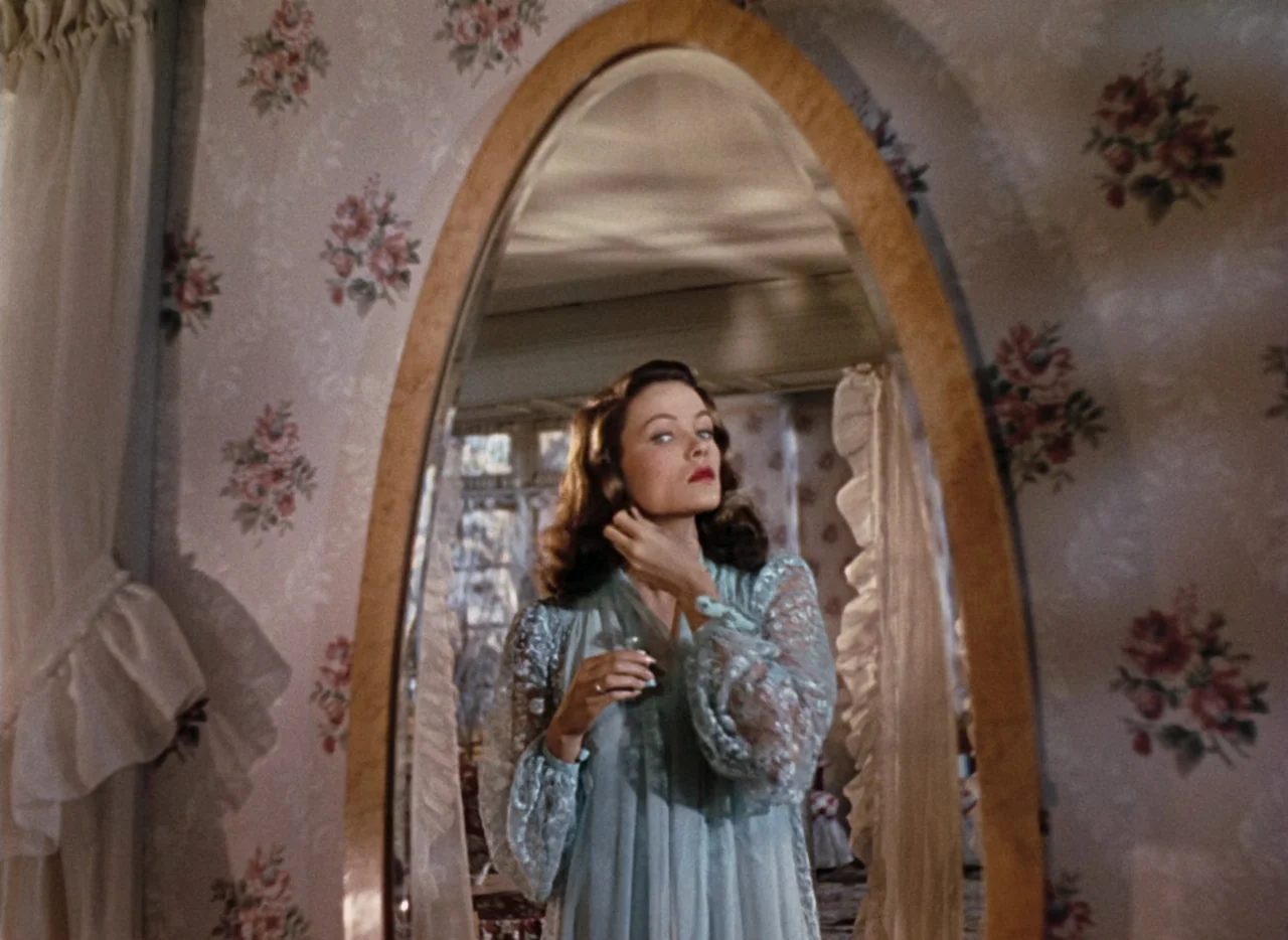 Leave Her To Heaven (1945) movie still: medium — A room with floral wallpaper and an oval vanity mirror in a wooden frame. A woman wearing a lace…