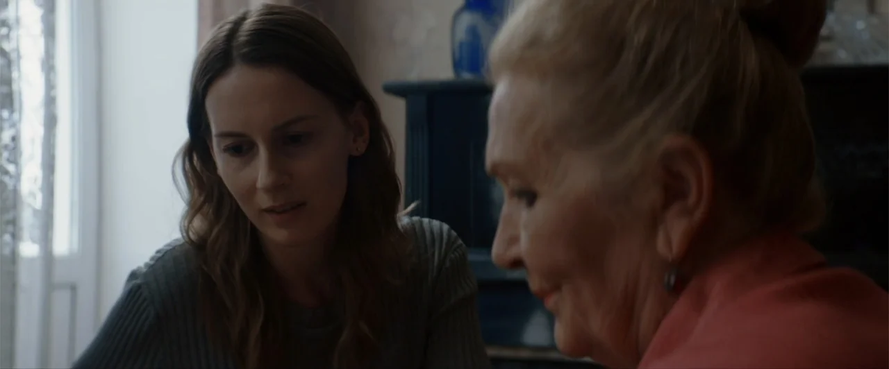 La herencia (2010) movie still: medium — A residential interior features a woman in a grey sweater facing an elderly woman. They are positioned in a…