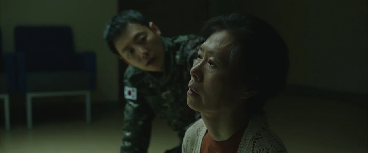 Along with the Gods: The Two Worlds (2017) movie still: medium — A dimly lit room provides a background for two individuals in low-key lighting. An…