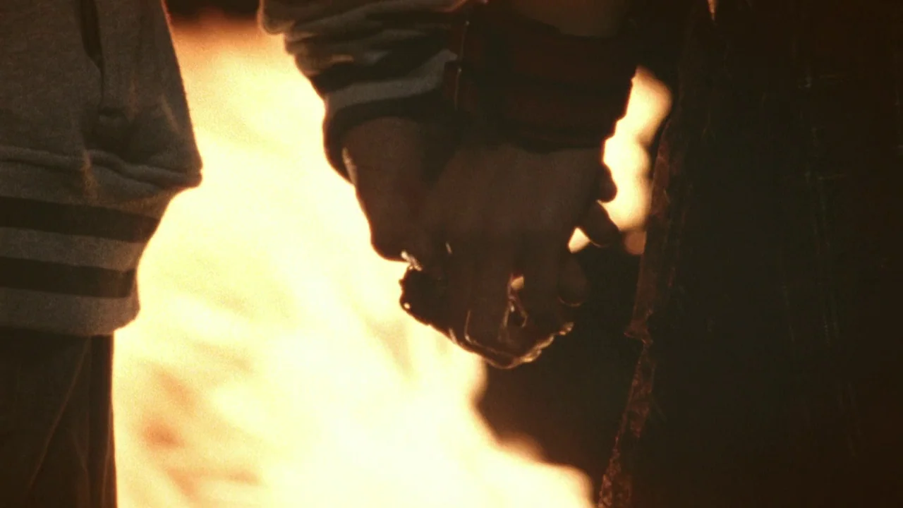 Confessions (2010) movie still: closeup — Two sets of hands are clasped together against the bright backdrop of a fire. The foreground subjects are…