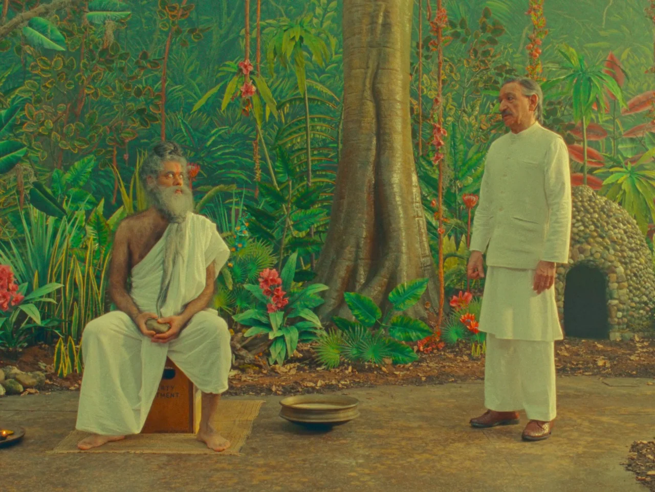 The Wonderful Story of Henry Sugar (2023) movie still: fullbody — A theatrical studio set features a painted jungle backdrop with a large tree…