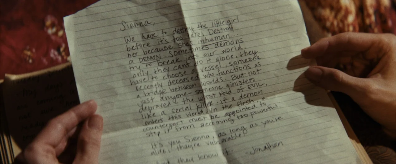 Terrifier 3 (2024) movie still: closeup — A lined piece of paper with handwritten text is held in two hands. The letter warns of demons and…