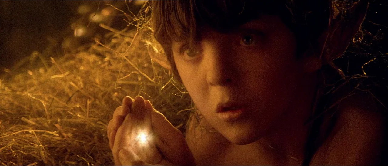 Legend (1985) movie still: closeup — A field of dry hay at night is illuminated by a small point of light. A young boy watches the light held in his…