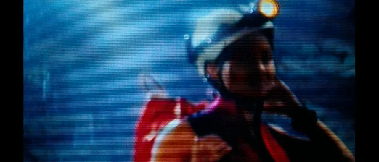 The Descent (2005) movie still: closeup — A dark, textured cave interior is illuminated by a single concentrated beam of light. A woman wearing a…