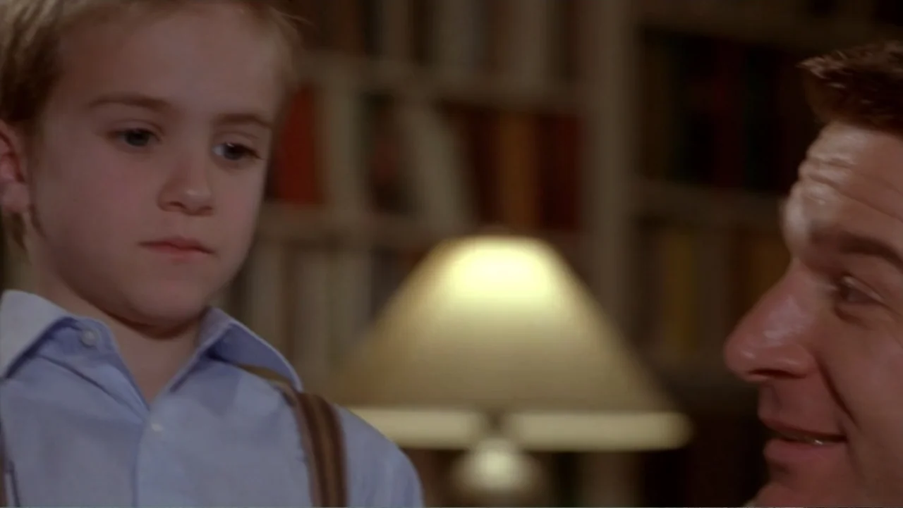 Music from Another Room (1998) movie still: medium — An interior study features bookshelves in the background and a lit desk lamp. A young boy faces…
