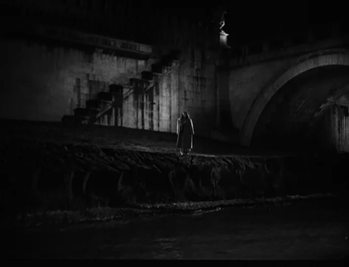 The White Sheik (1952) movie still: wide — A stone embankment wall rises above a dark river under a concrete arch bridge. A solitary woman in an…