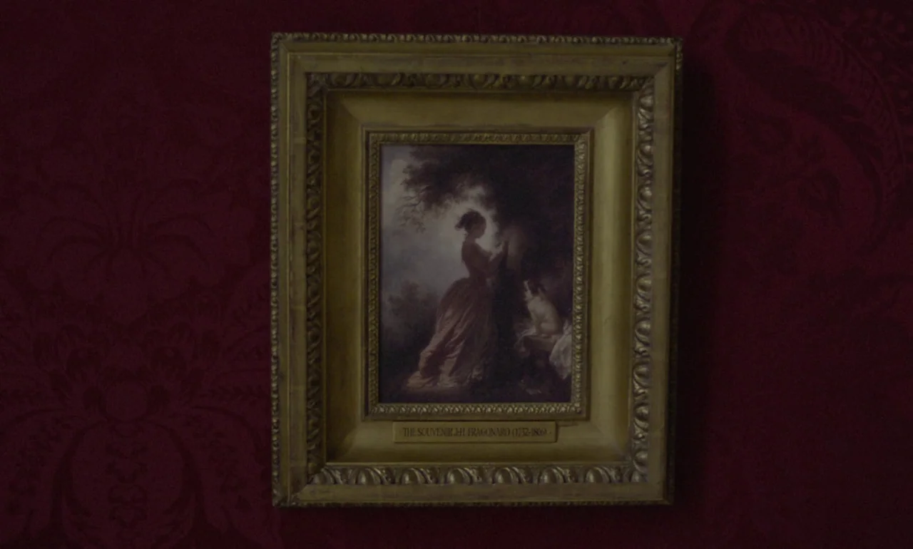 The Souvenir (2019) movie still: closeup — A dark red wall with patterned damask wallpaper features a framed historical oil painting. The painting…