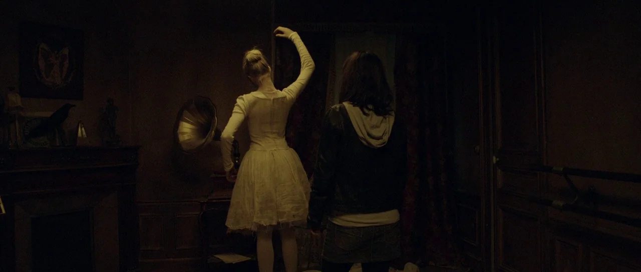 Livid (2011) movie still: fullbody — A dark, wood-paneled room is dimly lit with vintage furniture and a corner fireplace. A woman in a white…