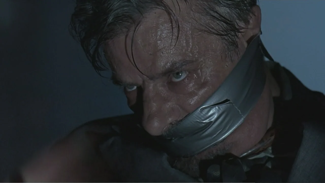 Hannibal (2001) movie still: closeup — A dark, dimly lit interior space serves as the setting for this close-up shot. A man with graying hair and…
