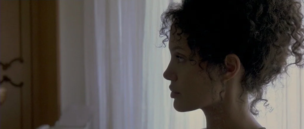 A Mighty Heart (2007) movie still: closeup — A bright room features sheer white curtains hanging in front of a window. A woman with dark curly hair…