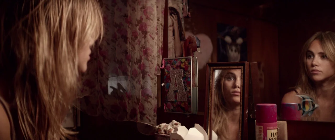 The Bad Batch (2016) movie still: medium — A cluttered personal vanity area features a small mirror reflecting a young woman's face. The wall is…