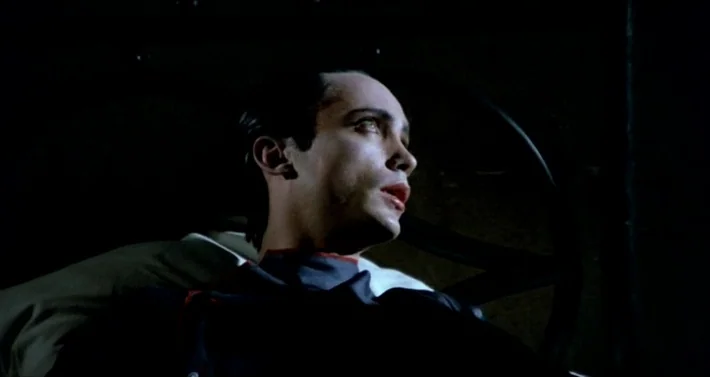 Blood For Dracula (1974) movie still: closeup — A dark, cramped interior space appears to be the inside of a vehicle. A man with slicked hair gazes…