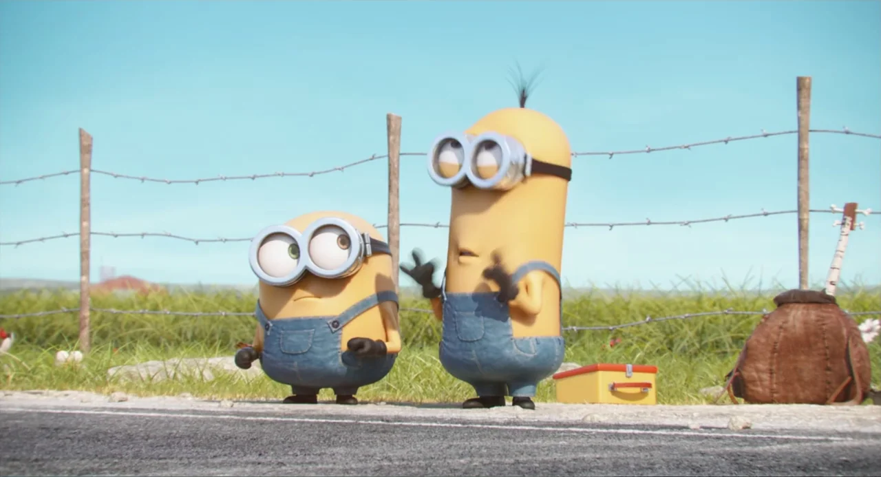 Minions (2015) movie still: medium — A rural roadside scene features a wire fence against a grassy landscape. Two yellow creatures stand on the…