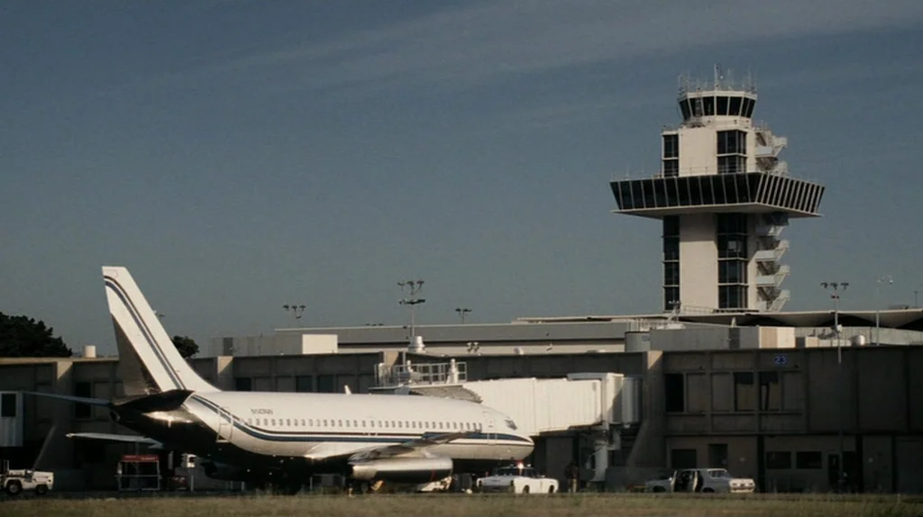 The Assassination of Richard Nixon (2004) movie still: wide — An airport tarmac features a parked commercial airliner connected to a terminal…