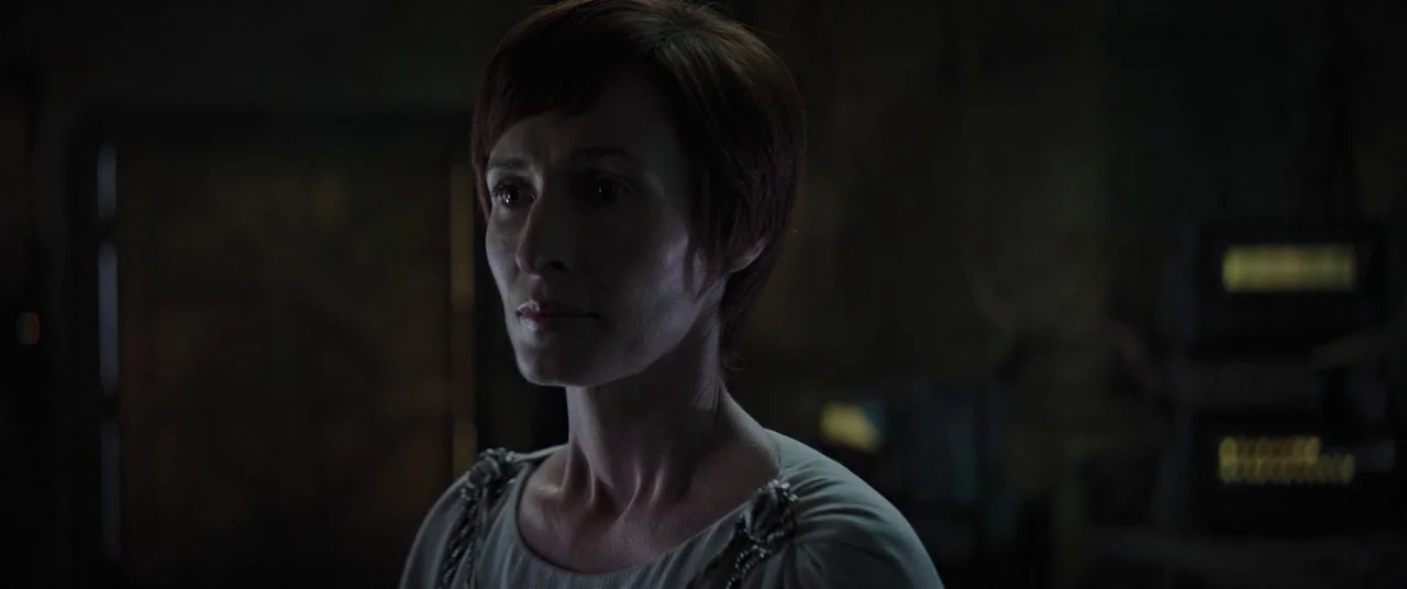 Rogue One: A Star Wars Story (2016) movie still: medium — A dimly lit room with industrial control equipment in the dark background. A woman stands…