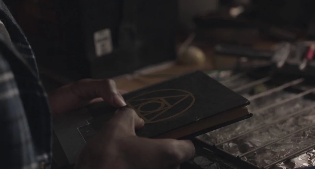 The Alchemist Cookbook (2016) movie still: closeup — A cluttered workshop workbench contains various metal tools and reflective metallic surfaces. A…