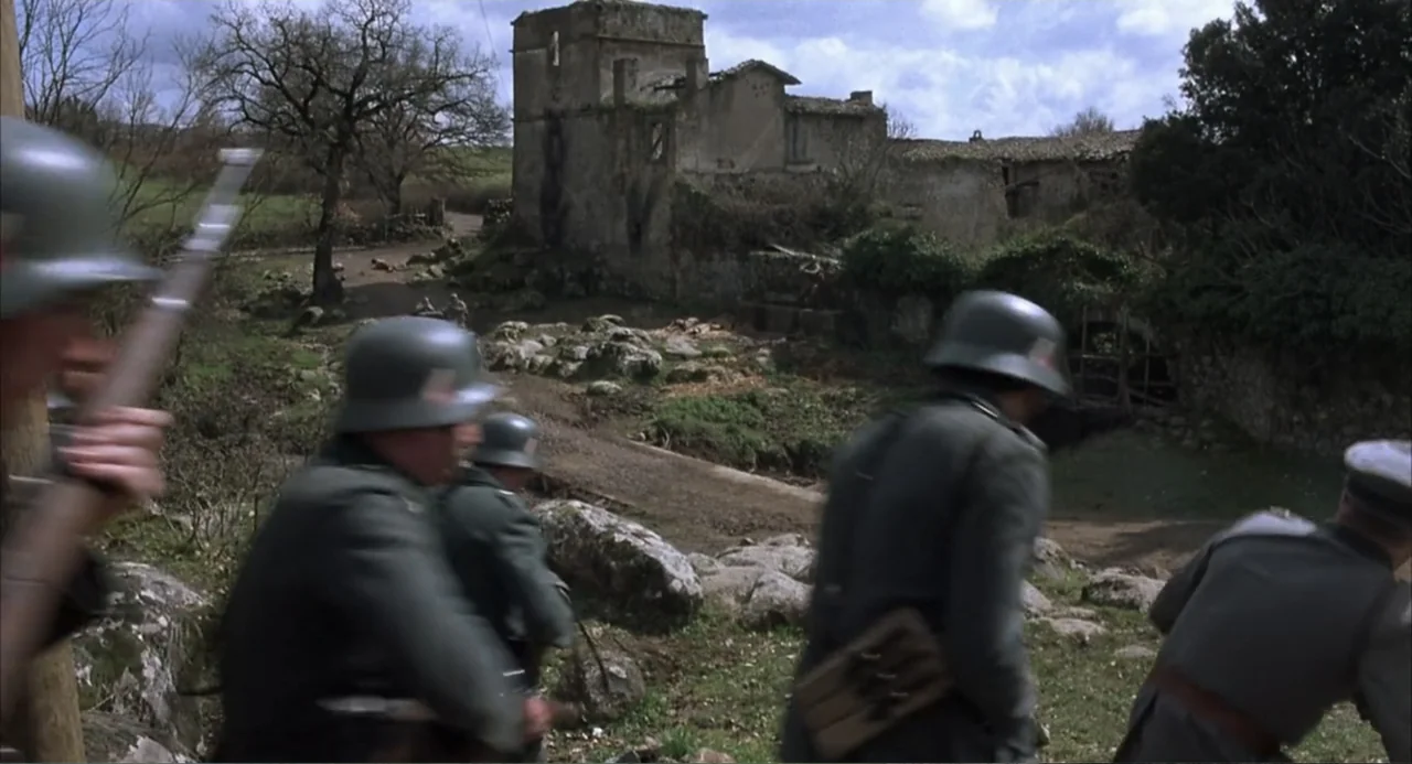 Zone Troopers (1985) movie still: fullbody — A rural landscape featuring a derelict stone tower structure amidst boulders and grass. A small group…