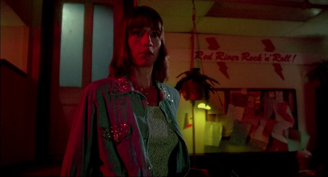 The Texas Chainsaw Massacre 2 (1986) movie still: medium — A dimly lit room features a notice board with the text Red River Rock'n'Roll. A woman…