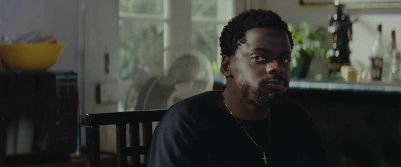 Queen & Slim (2019) movie still: medium — A well-lit residential dining room features a window with an electric fan nearby. A young black man sits…