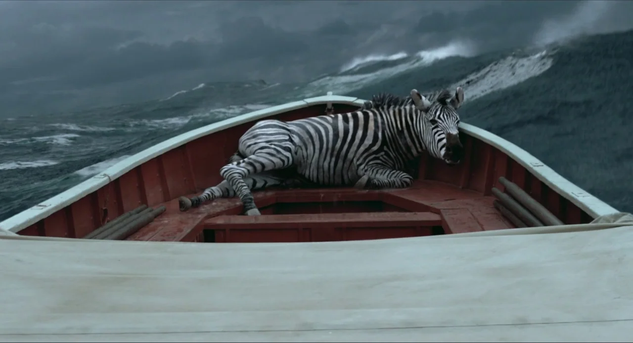 Life of Pi (2012) movie still: medium — A zebra lies in the wooden bow of a red boat on a turbulent sea. Stormy gray waves crest high around the…