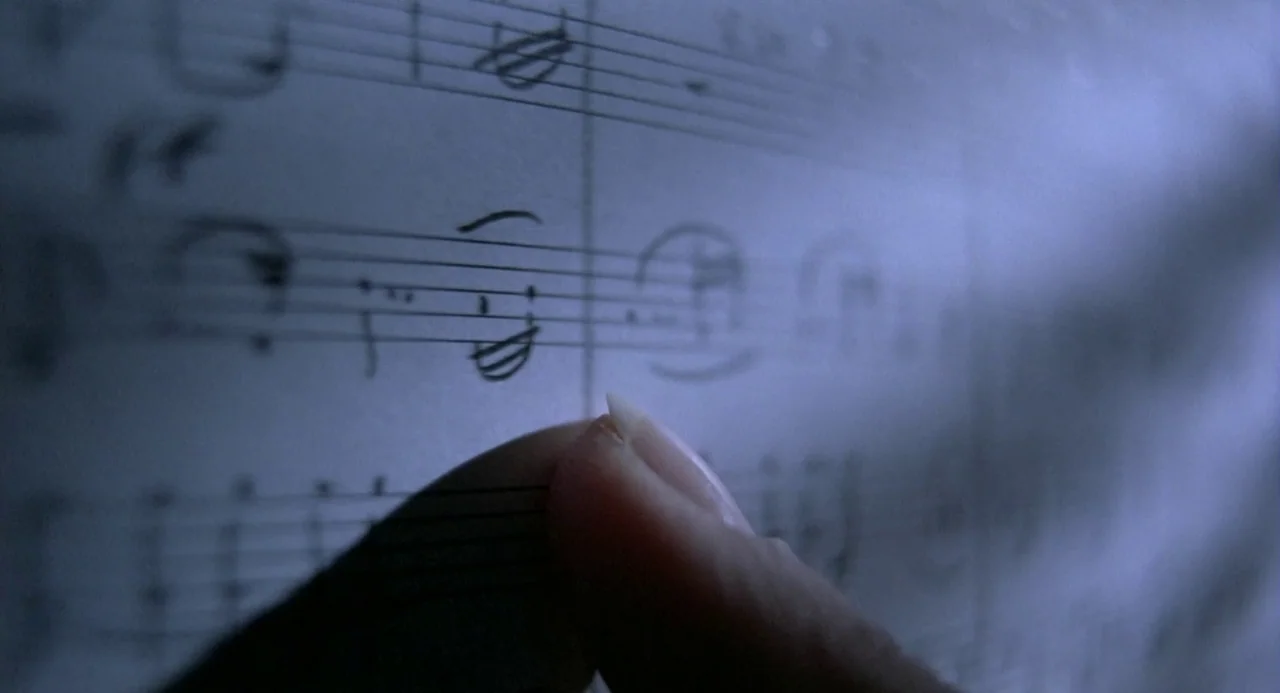 Three Colours: Blue (1993) movie still: closeup — A close up shot of a handwritten musical score on paper. A single finger presses gently against…
