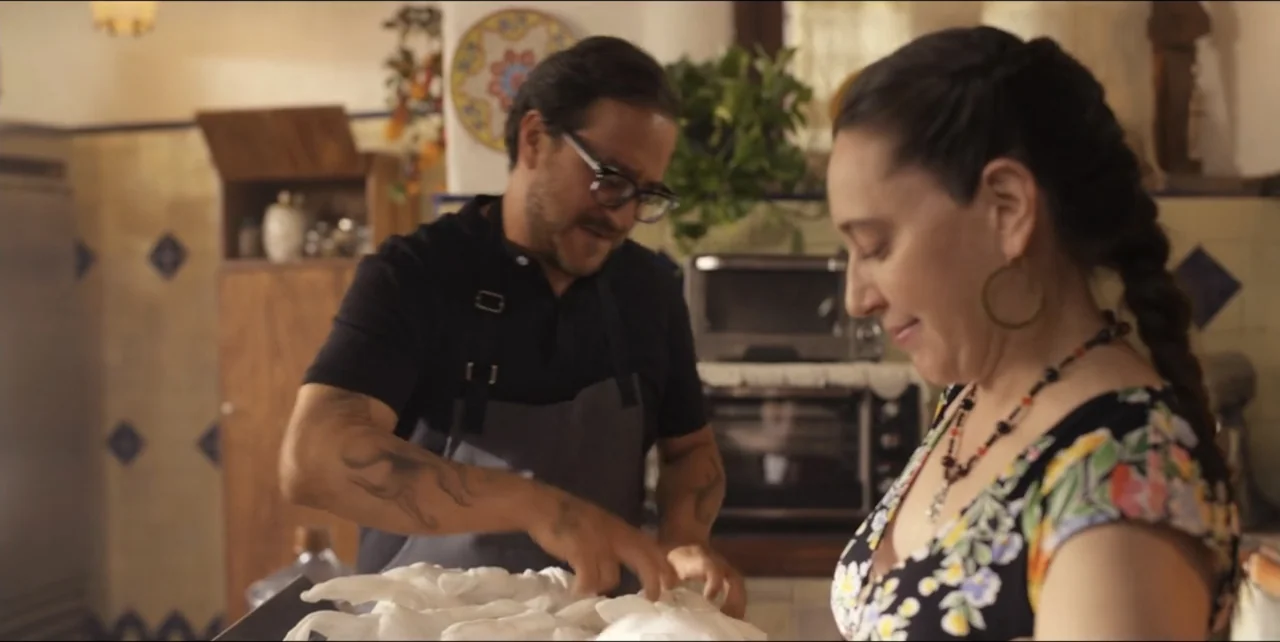 El sabor de la Navidad (2023) movie still: medium — A rustic home kitchen features tiled walls and various appliances in the background. A man and a…