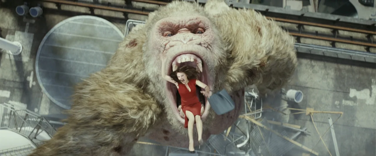 Rampage (2018) movie still: medium — A high-angle view looks down at a large ape clutching a woman in red. The scene takes place above a city street…