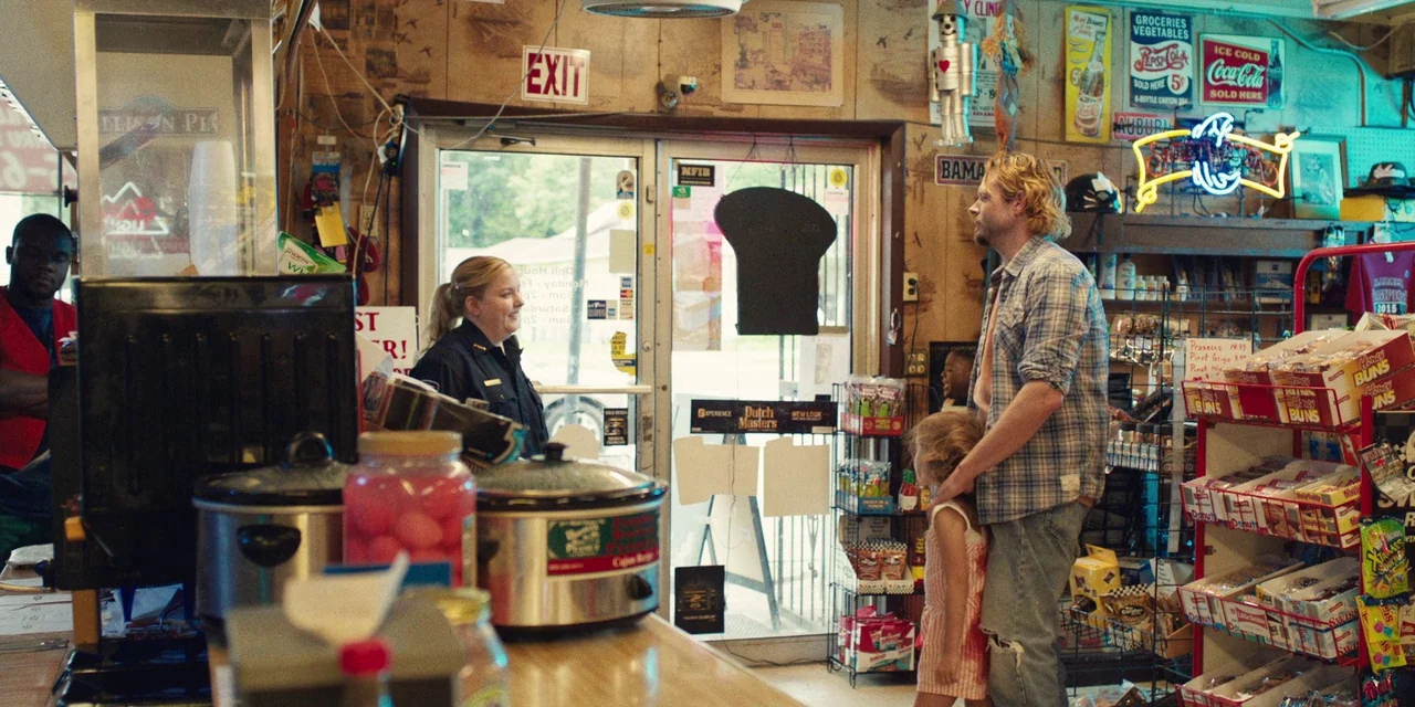 The Death of Dick Long (2019) movie still: medium — A rustic shop interior with wood-paneled walls covered in vintage advertisements and neon signs.…