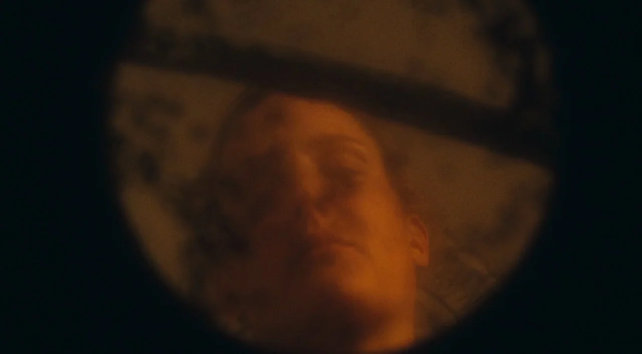 Phantom Thread (2017) movie still: closeup — A view through a circular peephole lens in a dark environment. A woman's face is partially visible…