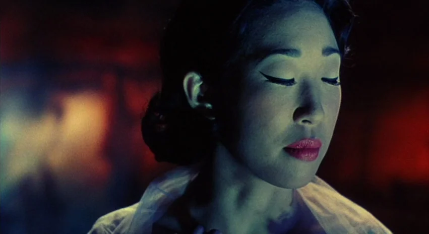 Double Happiness (1994) movie still: closeup — A dark, minimally lit interior space with a blurred red background. A young woman with her eyes…