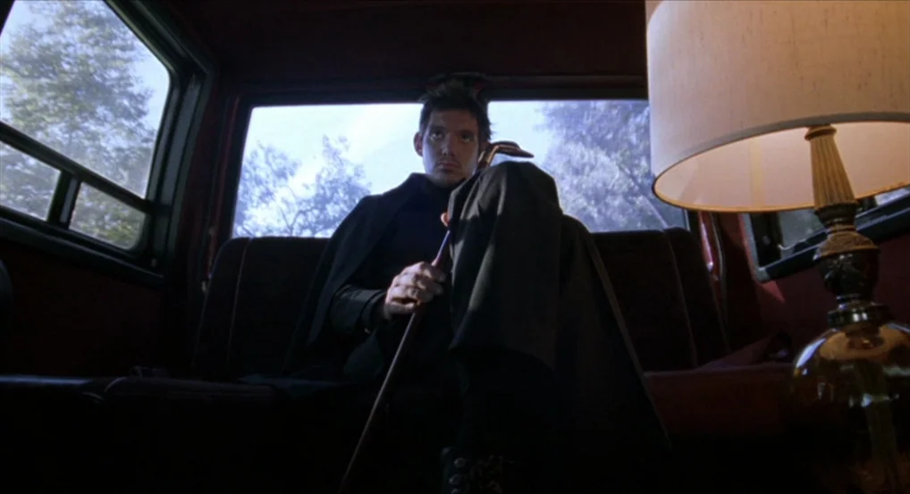 Brick (2005) movie still: medium — A dark vehicle interior features dark leather bench seating and a nearby table lamp. A man sits in the middle of…