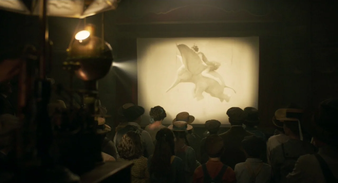 Dumbo (2019) movie still: medium — An audience watches a flickering animated projection of a flying elephant inside a dark venue. The crowd is seen…