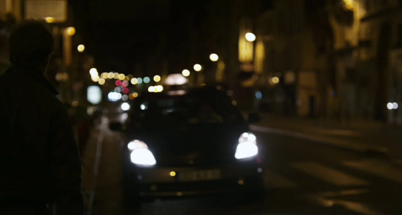 Bastards (2013) movie still: medium — A dark city street at night illuminated by the bright headlights of an oncoming car. The person in the…