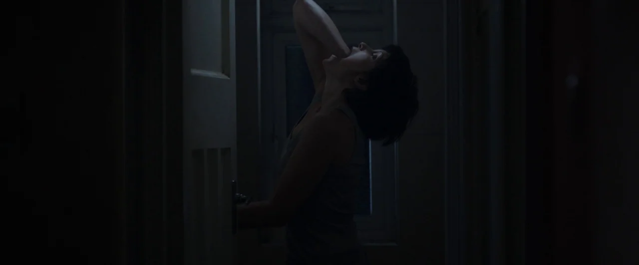 You Are Not My Mother (2021) movie still: medium — A dark, dimly lit domestic hallway with a window visible in the background. A woman in a tank top…