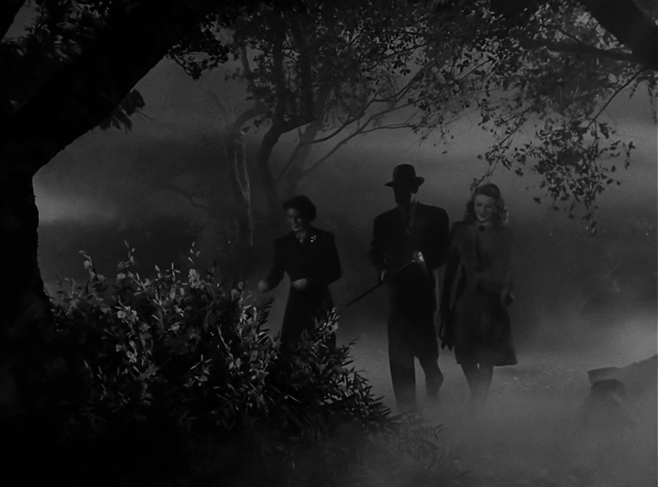 The Wolf Man (1941) movie still: wide — A dark, dense forest area is obscured by heavy rolling fog at night. Two women and one man walk side by side…