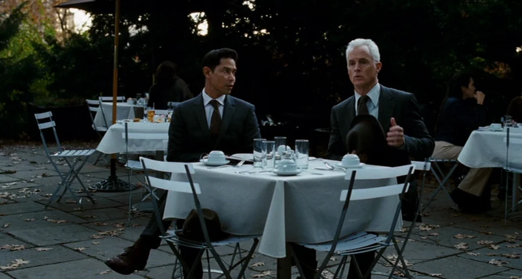 The Adjustment Bureau (2013) movie still: medium — An outdoor dining terrace features white-clothed tables set on stone paving with scattered…