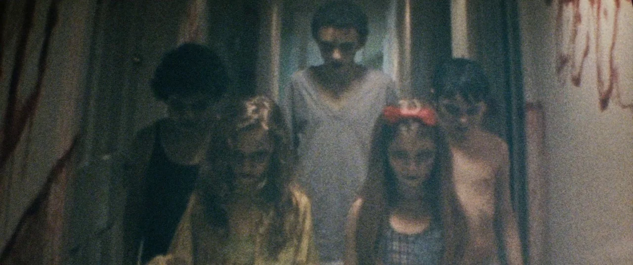 Sinister (2012) movie still: medium — A dark, narrow residential hallway with walls stained by dark red, irregular streaks. Five young individuals…