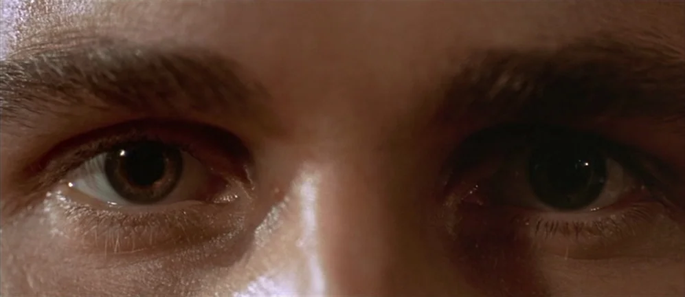 American Psycho (2000) movie still: closeup — A tight closeup focuses on the eyes of a young man. The subject gazes forward with clear, wide eyes in…