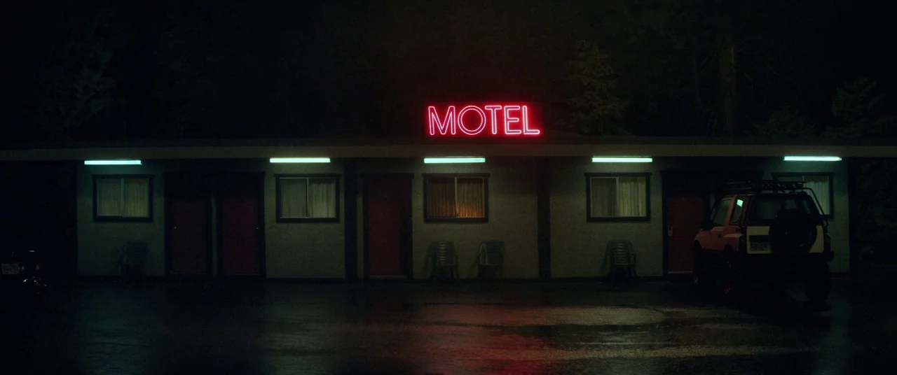 Come To Daddy (2019) movie still: establishing — A single-story motel building at night features a glowing red neon sign overhead. Several room…