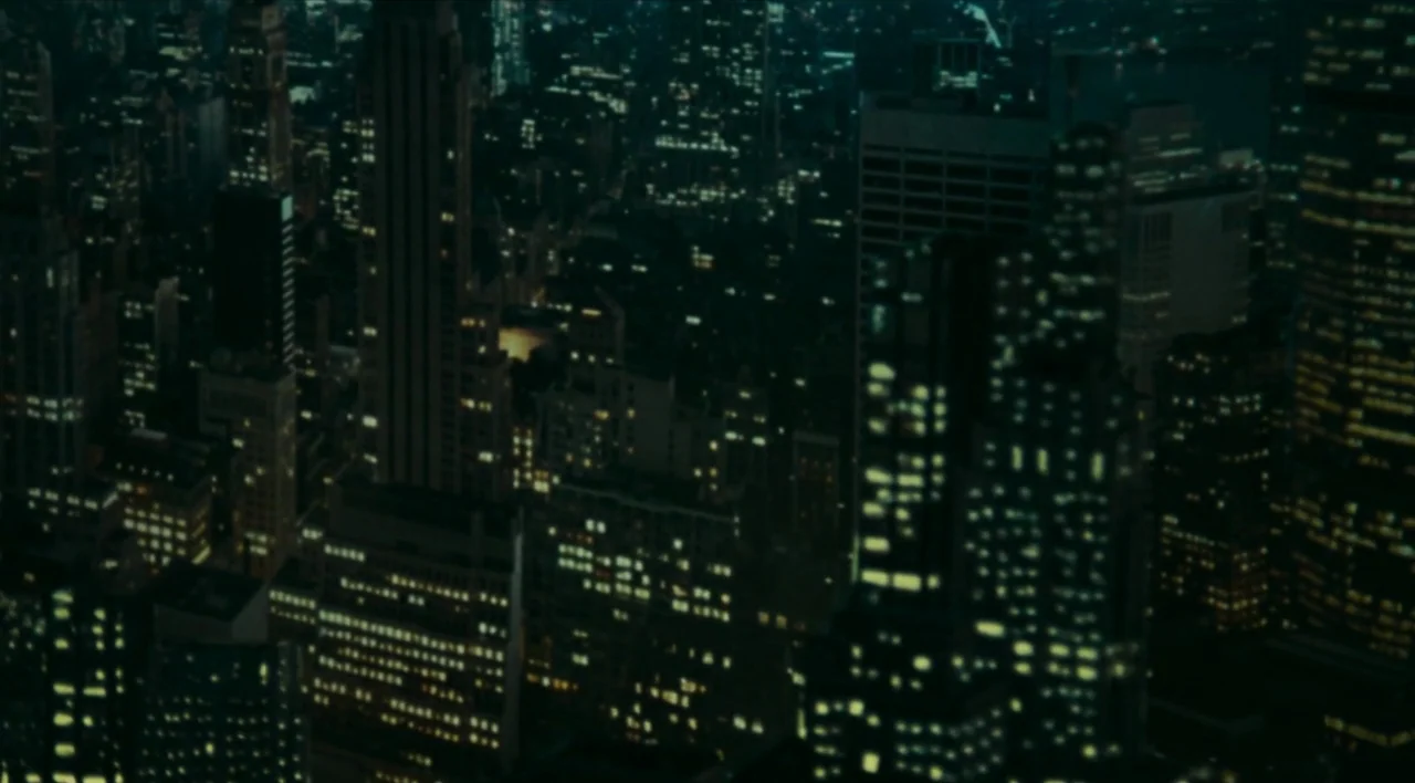 The Other Conquest (1999) movie still: establishing — An elevated view of a dense metropolitan urban center at night. Tall skyscrapers display…