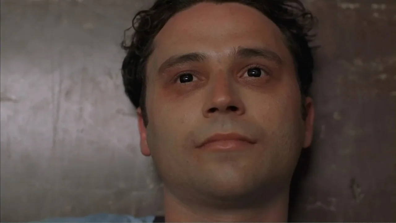 Day of the Dead 2: Contagium (2005) movie still: closeup — A man's face fills the frame against a flat, neutral brown textured wall. He stares…