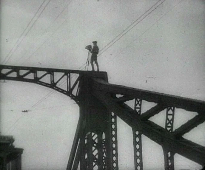 Man with a Movie Camera (1929) movie still: wide — A man stands on top of a massive steel bridge structure against a sky. The operator manages a…